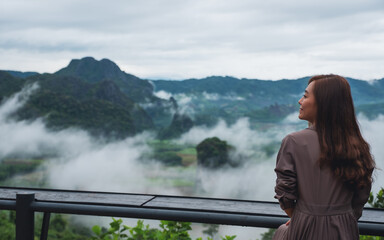 Fototapeta na wymiar Rear view image of a female traveler looking at a beautiful foggy mountain and nature view