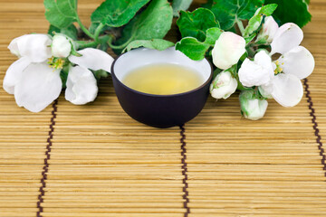 Green tea in a ceramic cup with branches of blossoming apple tree on a bamboo background. Copy space. Spring background.