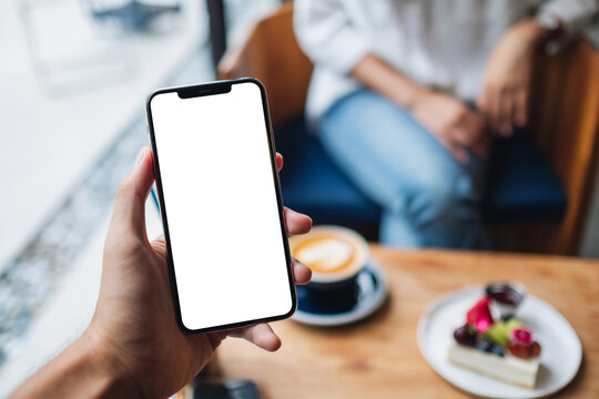 Mockup image of a man's hand holding mobile phone with blank white screen in cafe