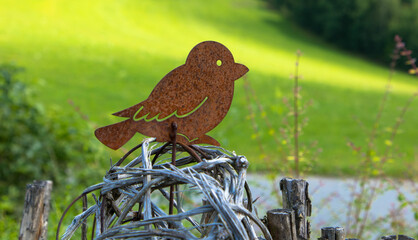 Garden decoration. A bird made of rusty sheet steel sits on a wooden fence. Space for text