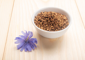 Chicory flower and sublimated root of chicory in white bowl on wooden table