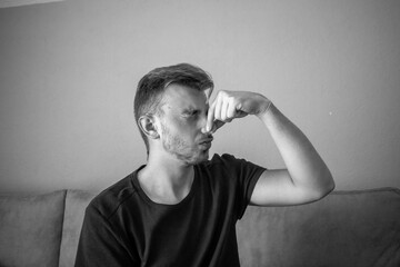 Black and White, Young man wearing a t-shirt keeping his nose shut because of a bad smell, odor.