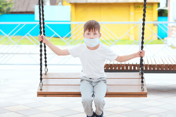 child in a mask on a swing. boy in a medical mask on the playground.