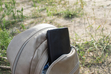 against the background of grass stands a backpack with a wallet sticking out of its pocket