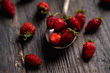 Red ripe wild strawberry in old vintage spoon on the rustic background. Selective focus. Shallow depth of field.
