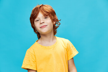 Red-haired child smiling on a blue background and a yellow T-shirt 