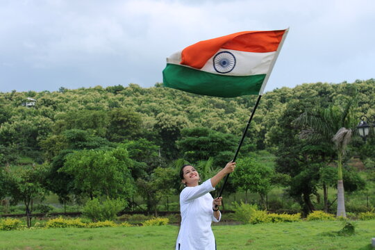 Beautiful Indian girl holding, waving or running with Tricolour with greenery in the background, celebrating Independence or Republic day.