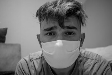 Young male with light brown hair wearing a white medical mask having a devastated and worried look...
