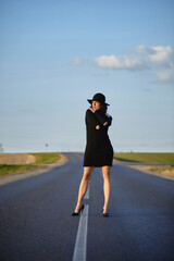 attractive girl in black dress and hat posing on the road with a dividing strip