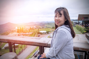 Elderly asian girl are sitting on wooden chair on the mountain for looking beautiful view at prtchabun province , Thailand.