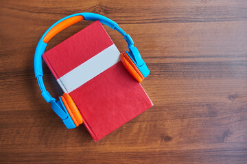Audio book concept. Headphones and red book on a wooden table. Top view with space for your text....