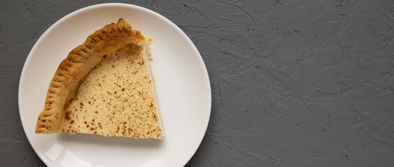 Piece of Homemade Sugar Cream Pie on a white plate on a gray surface, top view. Flat lay, overhead, from above. Space for text.