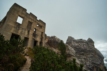 An old abandoned mountain hut on the edge of a rocky cliff face surrounded by thick fog, trees and mountains. Captured on the mountain of Monte Cristallo in the alpine region of Cortina, South Tyrol.