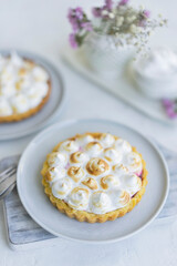 Mini tartlet with fruit jam and meringue. Tart with Italian meringue and cream on white plate on table. Selective focus, copy space, close up view. Homemade desert, beautiful breakfast. 