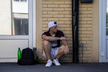 Young male with a red shirt and a white snap-back leaning on a yellow wall