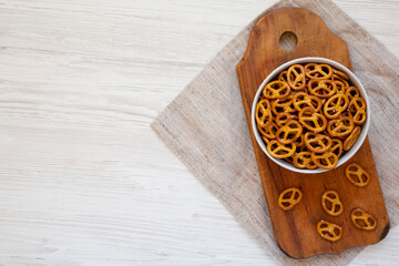 Crispy Pretzel Crackers in a Gray Bowl on a white wooden surface, top view. Flat lay, overhead, from above. Copy space.