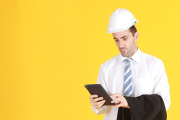 Handsome and smart engineer in suit and white shirt and Wearing a white safety engineer hat with hand holding smartphone isolated on yellow background. Copy Space