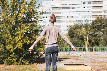 A young man stands with outstretched arms against the backdrop of a multi-storey building.