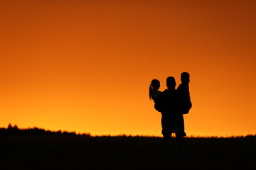 Fototapeta na wymiar beautiful sunset orange sky girls and dad happiness holding girls in his arms family