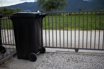 Black garbage container next to a fence AM