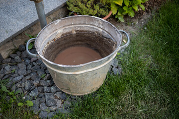 Fototapeta premium Metal bucket filled with water and dirt on the bottom of it in a park AM