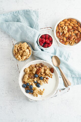 Yogurt with Granola. Breakfast, healthy diet food with oat flakes, nuts, banana, white table. Top view, copy space, vertical