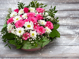 Beautiful pink roses and white daisies in a box on a gray wooden background.