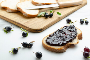 Morning breakfast.Slice of bread and blackcurrant jam, fresh sweet berries, wooden cutting board,knife on the white table