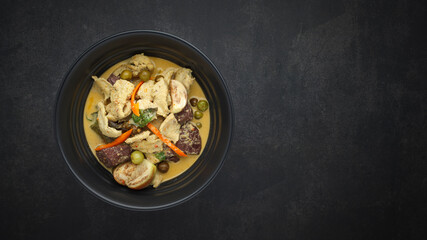 Thai traditional food sweet and spicy green curry with chicken, chicken blood curd, eggplant, small green aubergine, pea aubergine and coconut milk on dark texture background with copy space for text