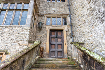 Old entrance wooden door with stone steps and mullioned windows.