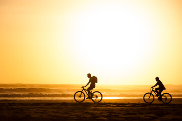 People walk and cycle on a beach during sunset