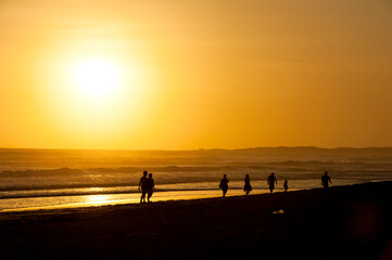 People walk and cycle on a beach during sunset