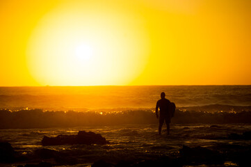 People walk and cycle on a beach during sunset