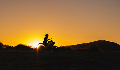 silhueta de homem a andar de moto nas montanhas ao pôr do sol