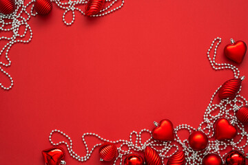 Red baubles and silver beads on the red background with copy space. Top view of various christmas ornaments. Happy new year flat lay.