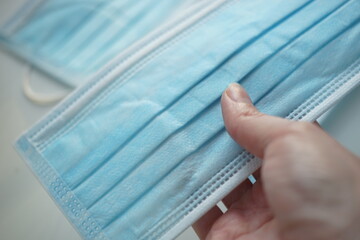 Female hand with blue medical face mask closeup.
