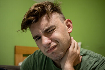 Fototapeta premium Young male with light brown hair having neck pain and holding his hand up his neck