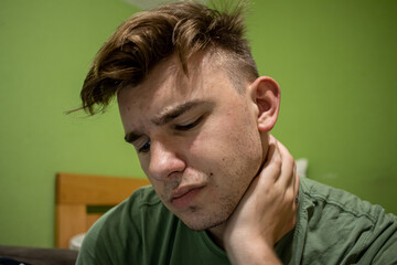 Fototapeta premium Young male with light brown hair having neck pain and holding his hand up his neck