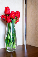 Red tulips stand on a shelf in a glass vase. Vertical view.