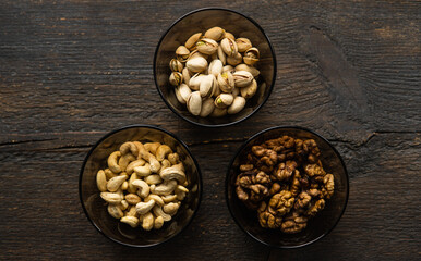 Walnut, pistachio and cashew in a small plates which standing on a black table. Nuts is a healthy vegetarian protein and nutritious food.
