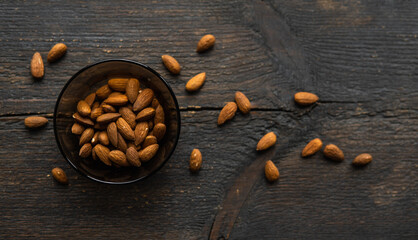 Almonds in a small plate with scattered nuts of almonds around a plate on a vintage wooden table as a background. Almond is a healthy vegetarian protein nutritious food. Natural nuts snacks.