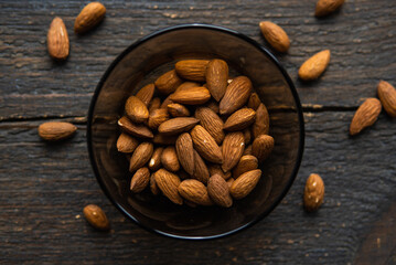 Almonds in a small plate with scattered nuts of almonds around a plate on a vintage wooden table as a background. Almond is a healthy vegetarian protein nutritious food. Natural nuts snacks.