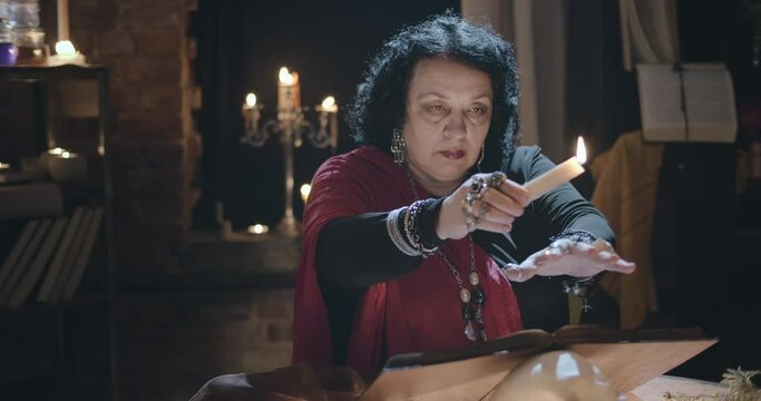 Old witch casting spell using candle wax and reading open book
