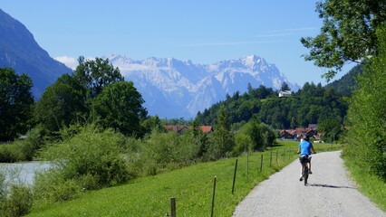 Fototapeta na wymiar Radlerin auf dem Loisach Fernradweg in Richtung Garmisch-Partenkirchen mit Loisach und Zugspitzmassiv, Bayern