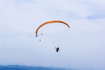 Paraglider flying against the blue sky with colorful wing above the clouds.