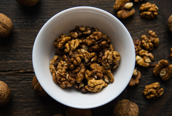 Walnut in a smale plate with scattered shelled nuts and whole nut which standing on a wooden vintage table. Walnuts is a healthy vegetarian protein nutritious food. Walnut on rustic old wood.