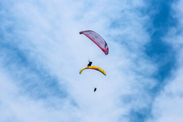Paraglider flying against the blue sky with colorful wing above the clouds.