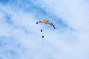 Paraglider flying against the blue sky with colorful wing above the clouds.
