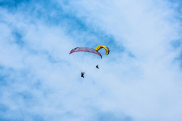 Paraglider flying against the blue sky with colorful wing above the clouds.