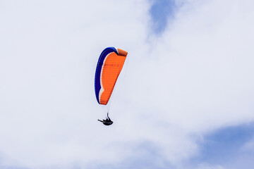 Paraglider flying against the blue sky with colorful wing above the clouds.
